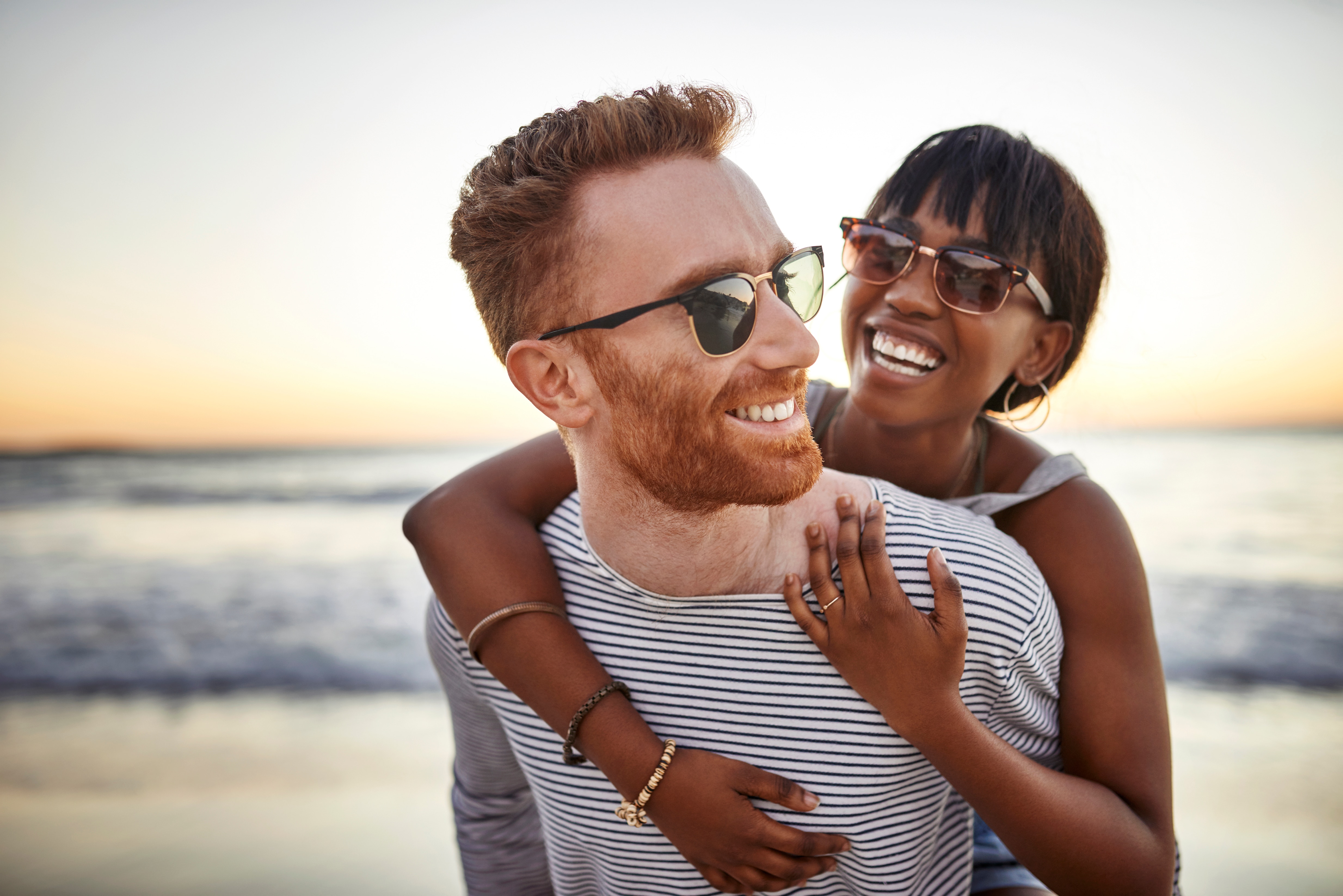 Couple in sunglasses smiling with the woman hugging her partner's shoulders