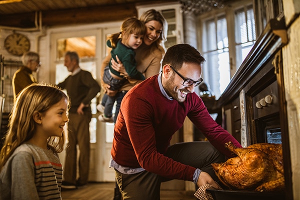 Family watching a man take a turkey out of oven