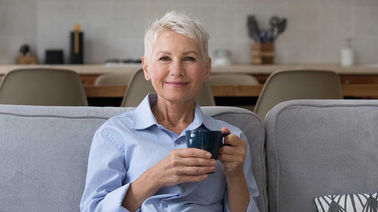 Senior woman sitting on sofa, holding coffee mug