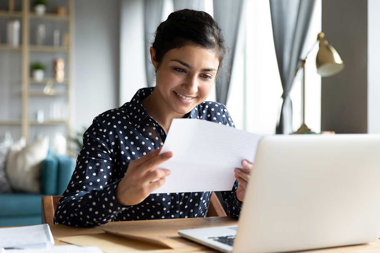 Woman comparing sheet of paper against laptop screen