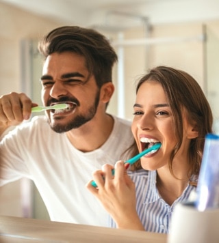 Man and woman brushing their teeth in a bathroom mirror