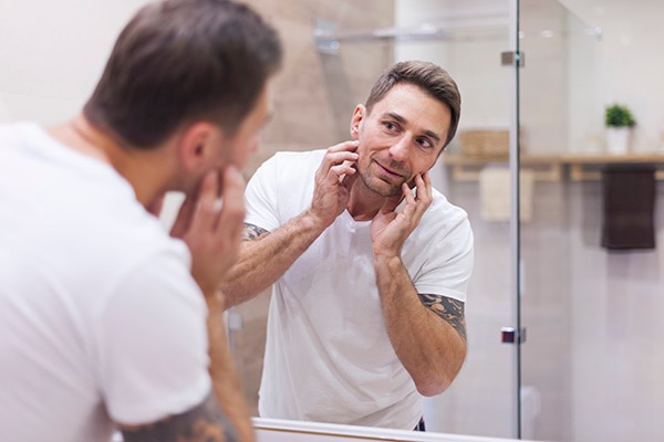 Man inspecting his face in a bathroom mirror