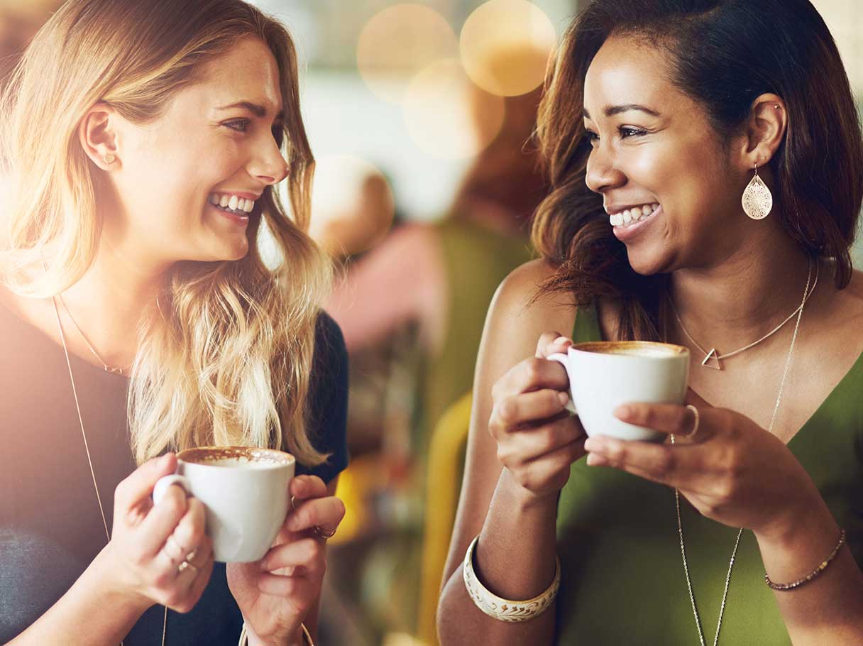 Two women smiling together as they drink coffee