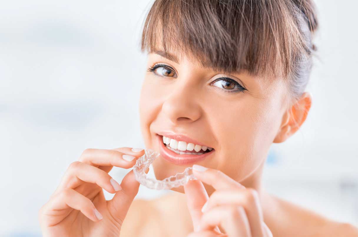 Woman holding an Invisalign retainer in front of her mouth