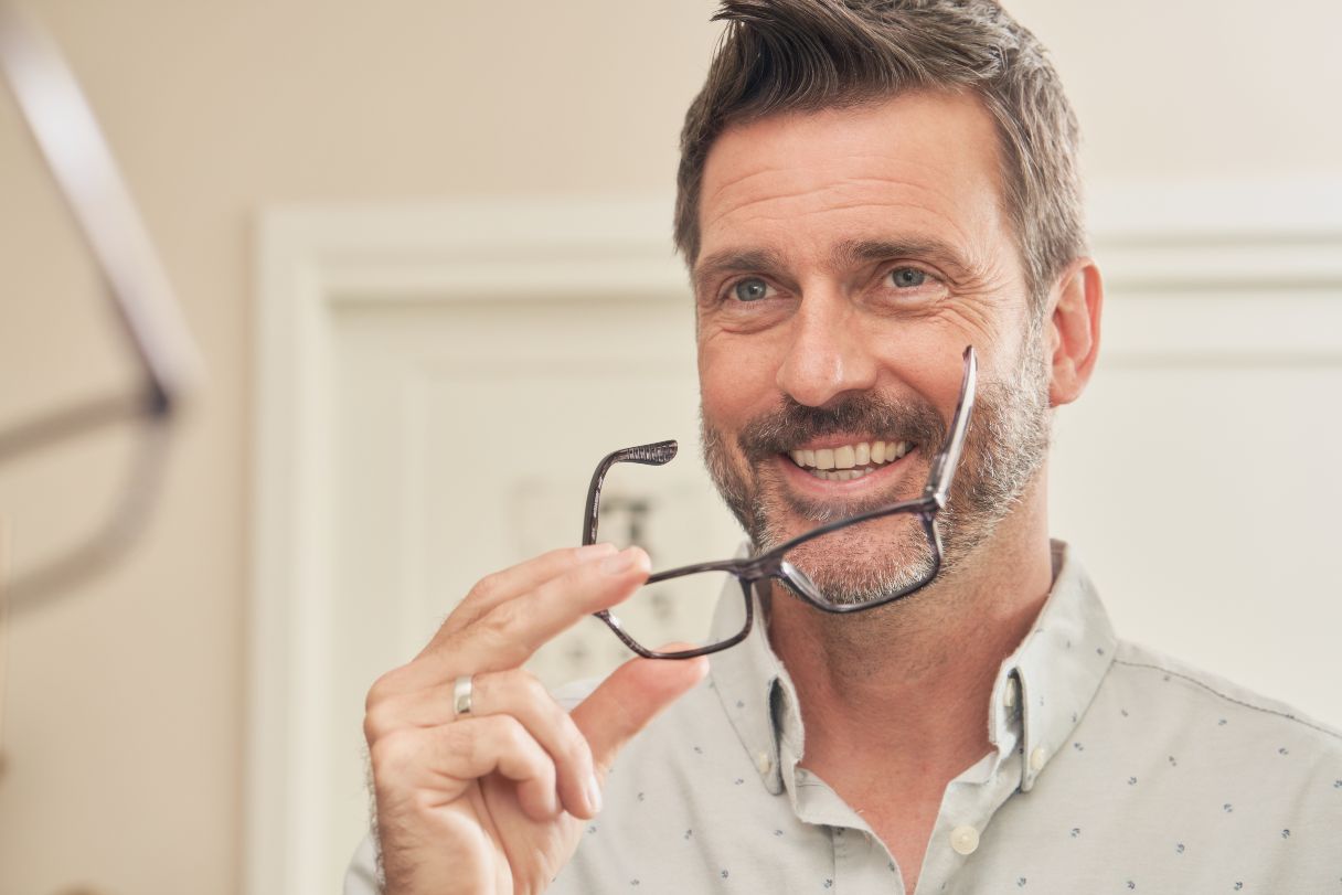 Smiling man with glasses looking into a mirror