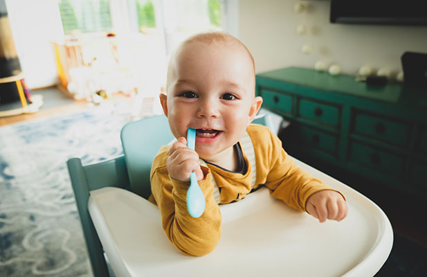 Baby in a high chair, teething on a spoon