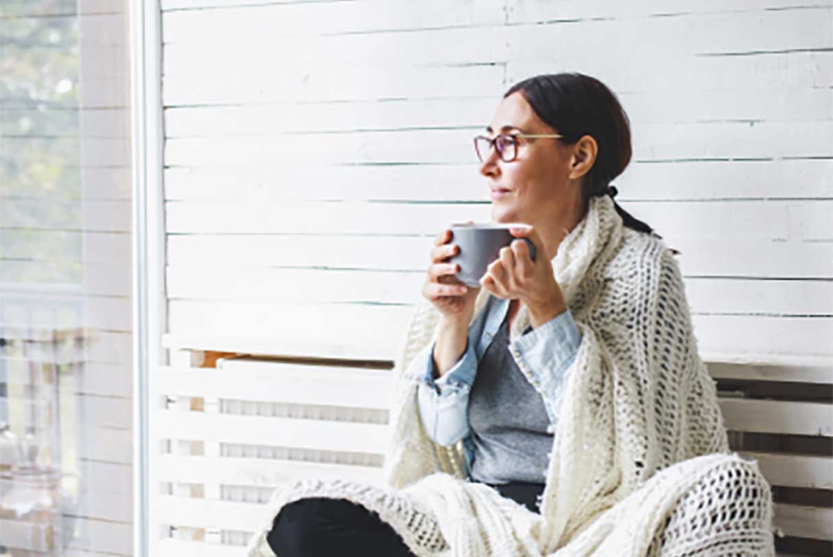 Woman bundled in blanket, drinking out of a coffee mug