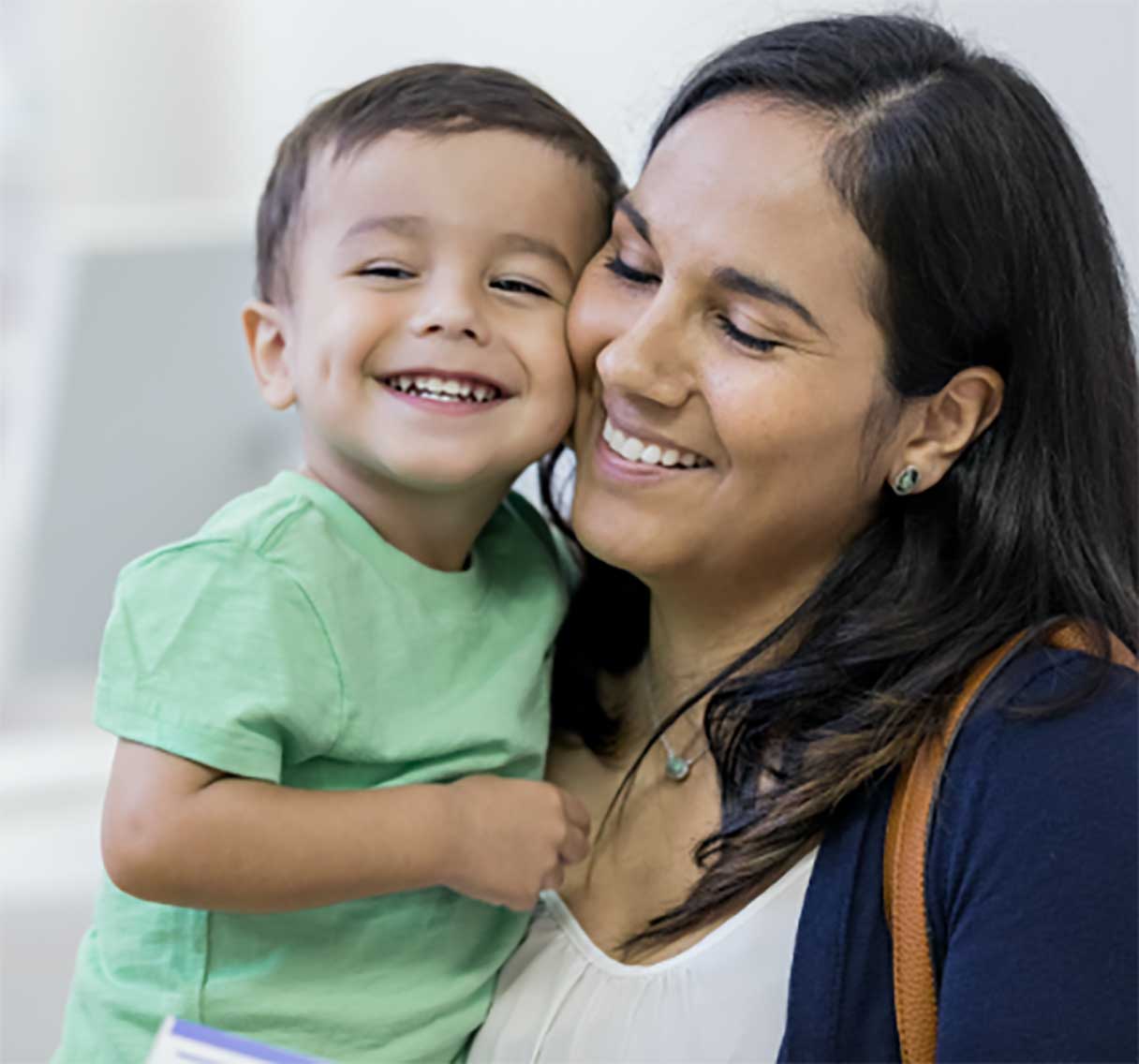 Woman holding toddler boy, both smiling cheek to cheek