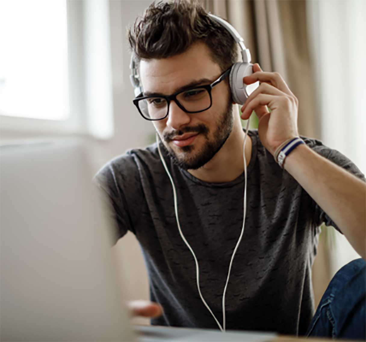 Man in glasses working on laptop with headphones on