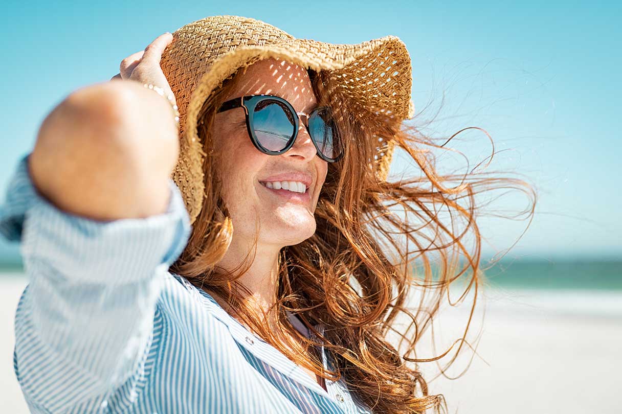 Woman with straw hat and sunglasses on smiling while standing on a beach