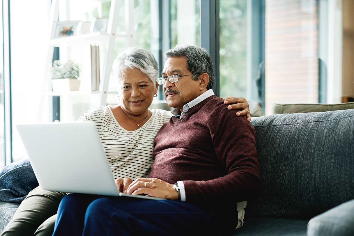 Senior couple, sitting on couch and looking at laptop