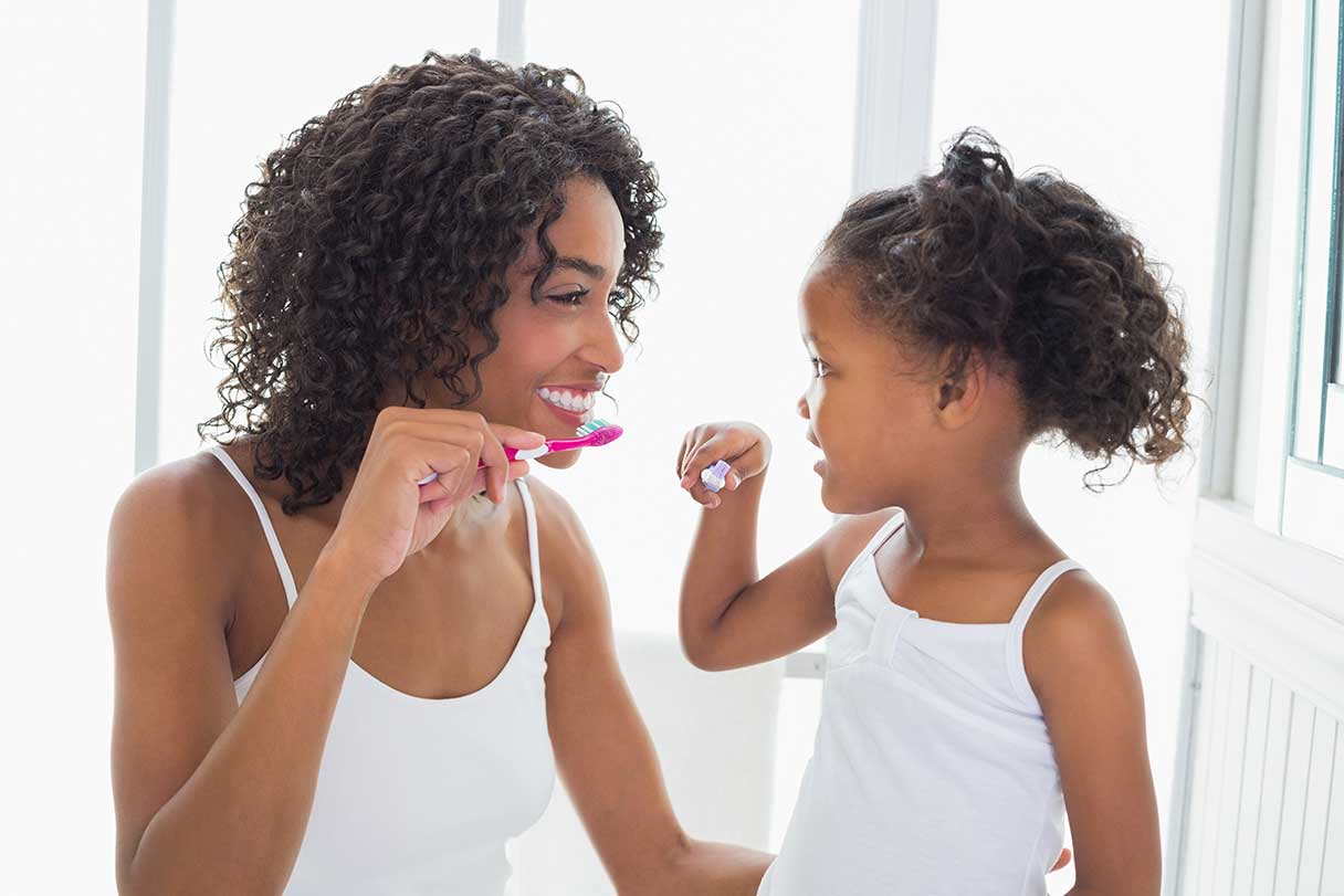 Woman and young girl brushing their teeth together