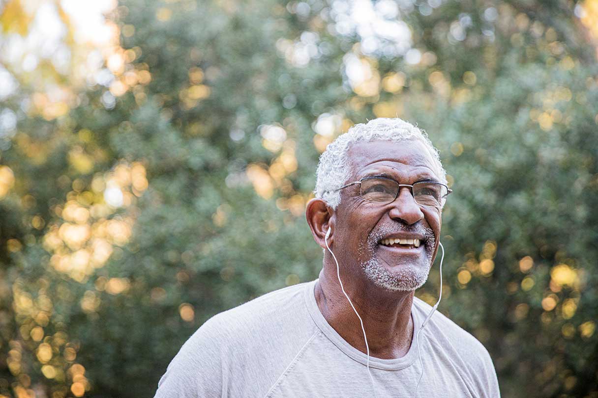 Senior man in glasses with headphones in, smiling while standing outside