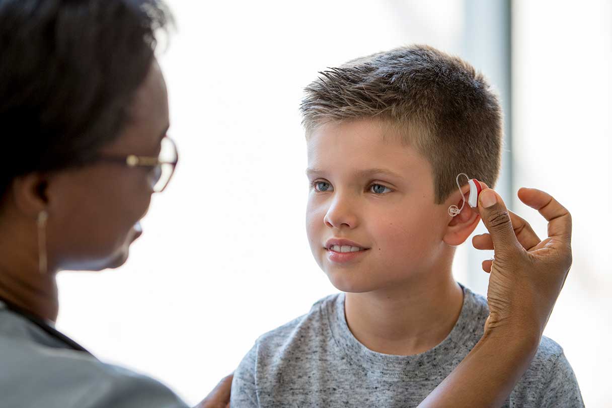 Woman inspecting young boy's hearing aid