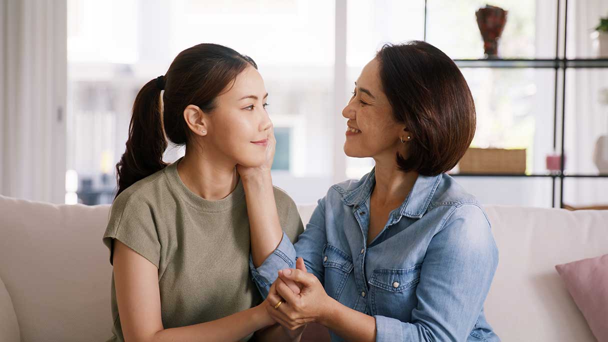 Woman smiling at young woman, both sitting on sofa