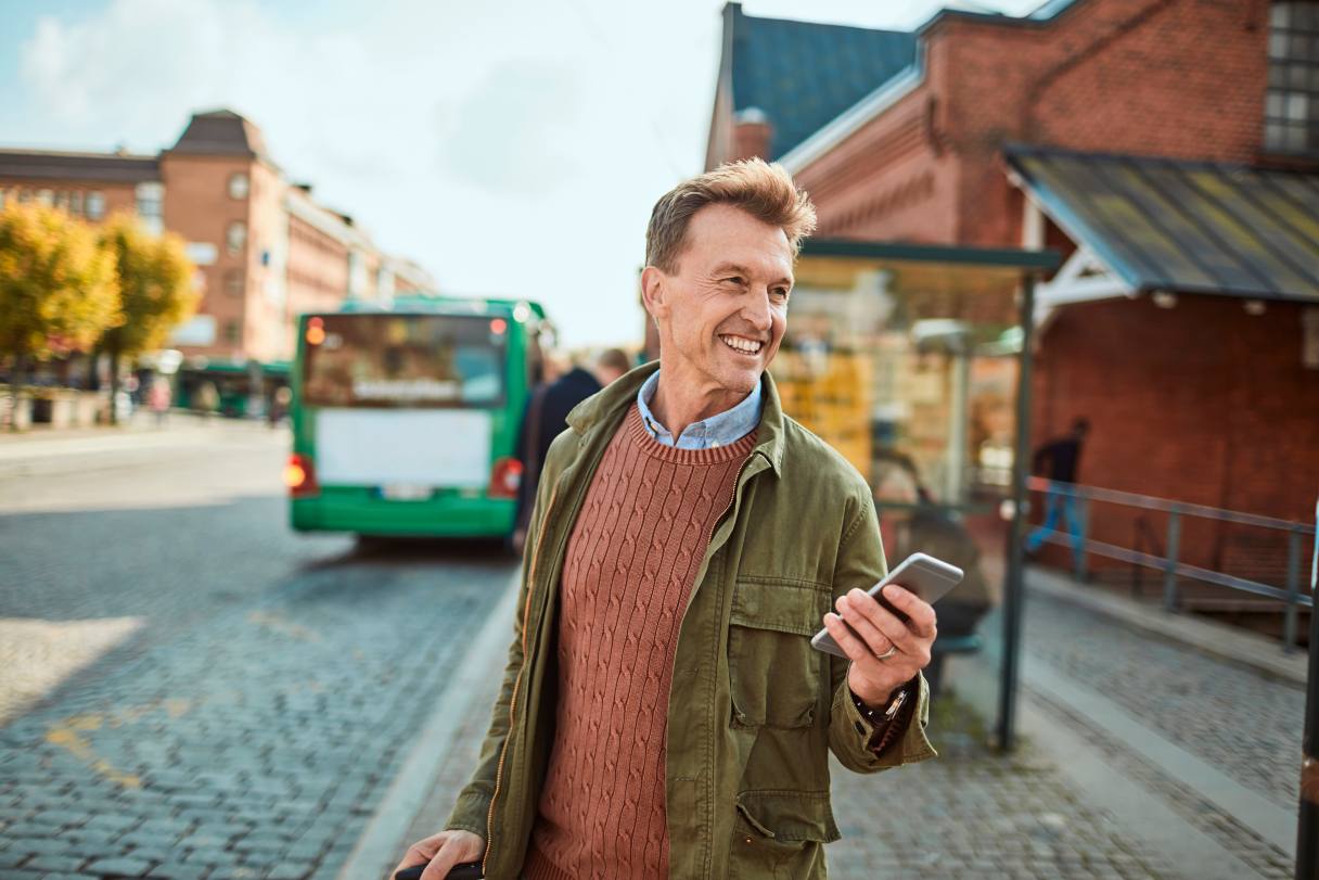 Smiling man holding mobile phone, standing in front of bus stop