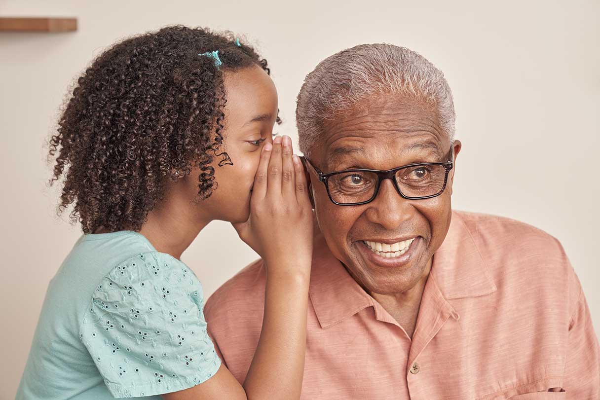 Young girl whispering into senior man's ear