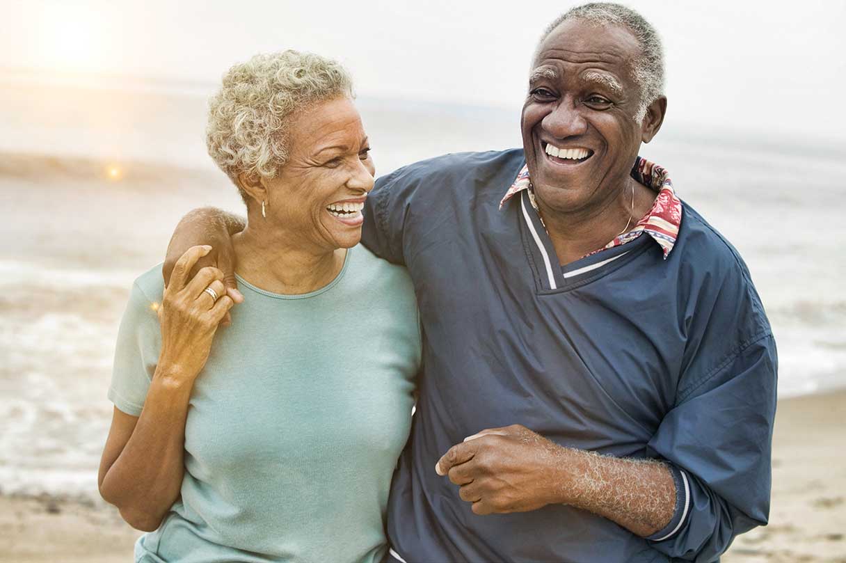 Senior man and woman walking together on a beach, both smiling