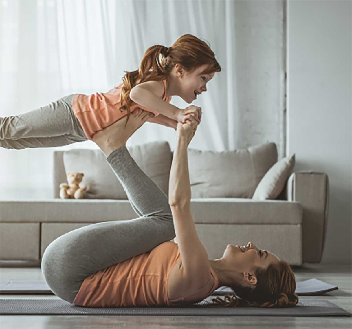 Woman on yoga mat, propping young girl up on her feet