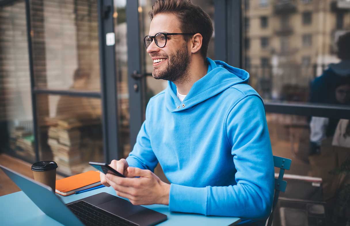 Man in eye glasses, smiling as he works on a laptop