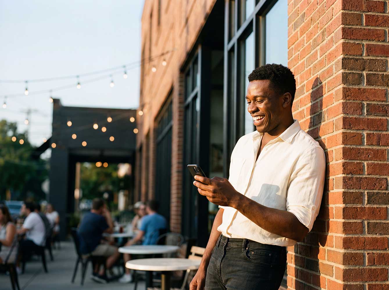 Man leaning against brick wall, looking down at phone
