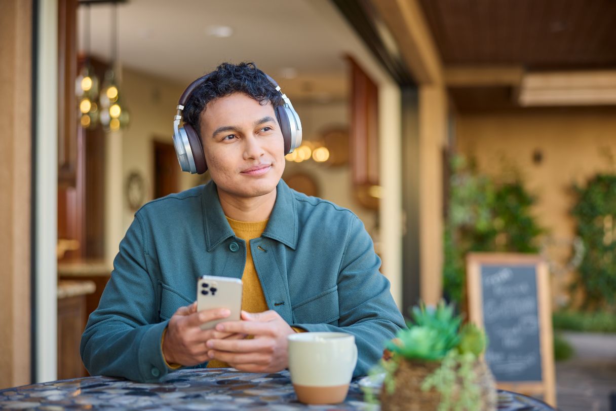 Man with headphones on sitting at cafe table, holding mobile device