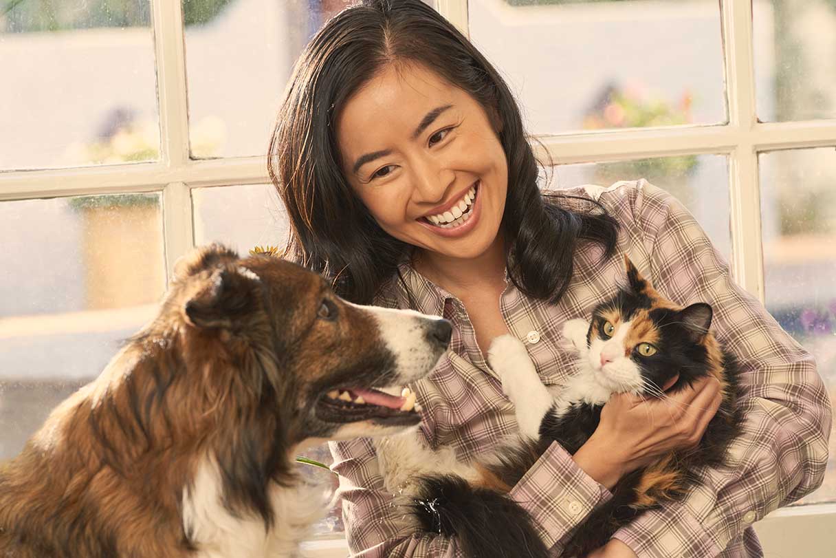 Smiling woman holding cat and looking at dog