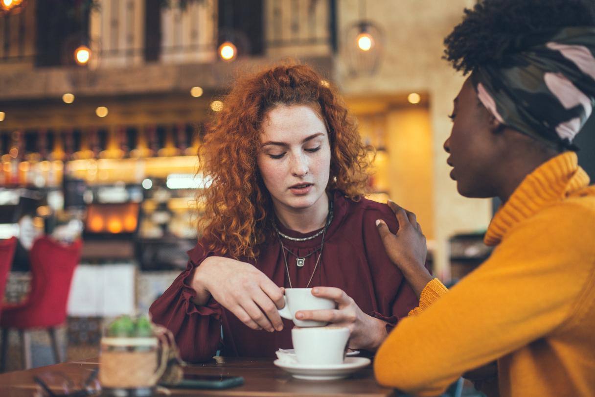 Two women sitting in a cafe, one comforting the other