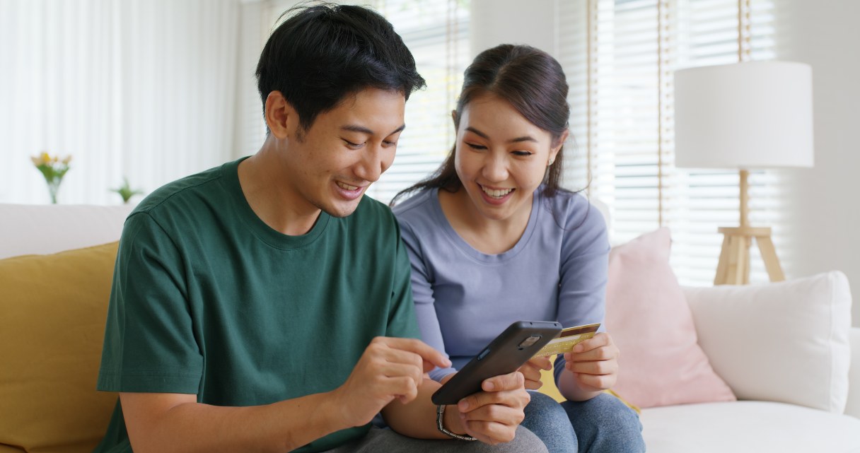Man and woman looking at mobile device, holding credit card