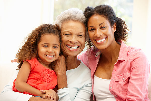 Young girl, senior woman, and young woman sitting side-by-side and smiling