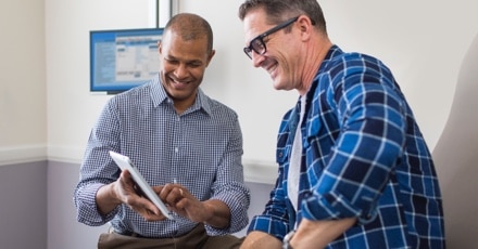 Two men smiling while one shows a tablet screen