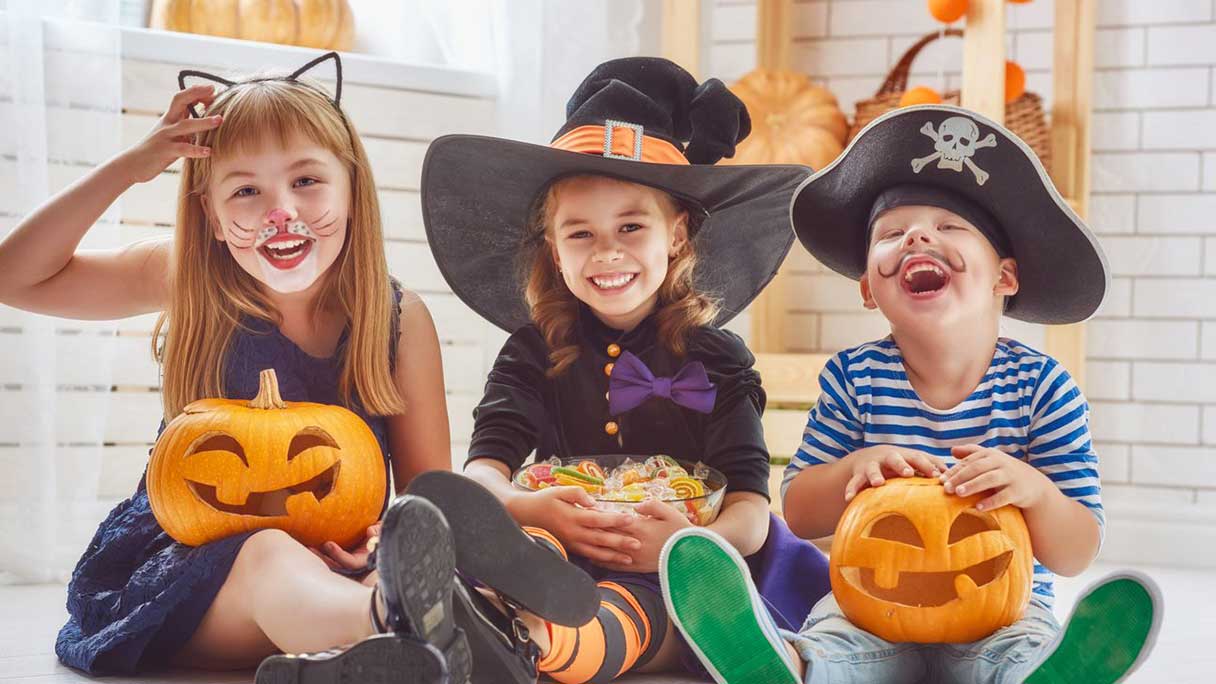 Three laughing children in Halloween costumes, holding candy