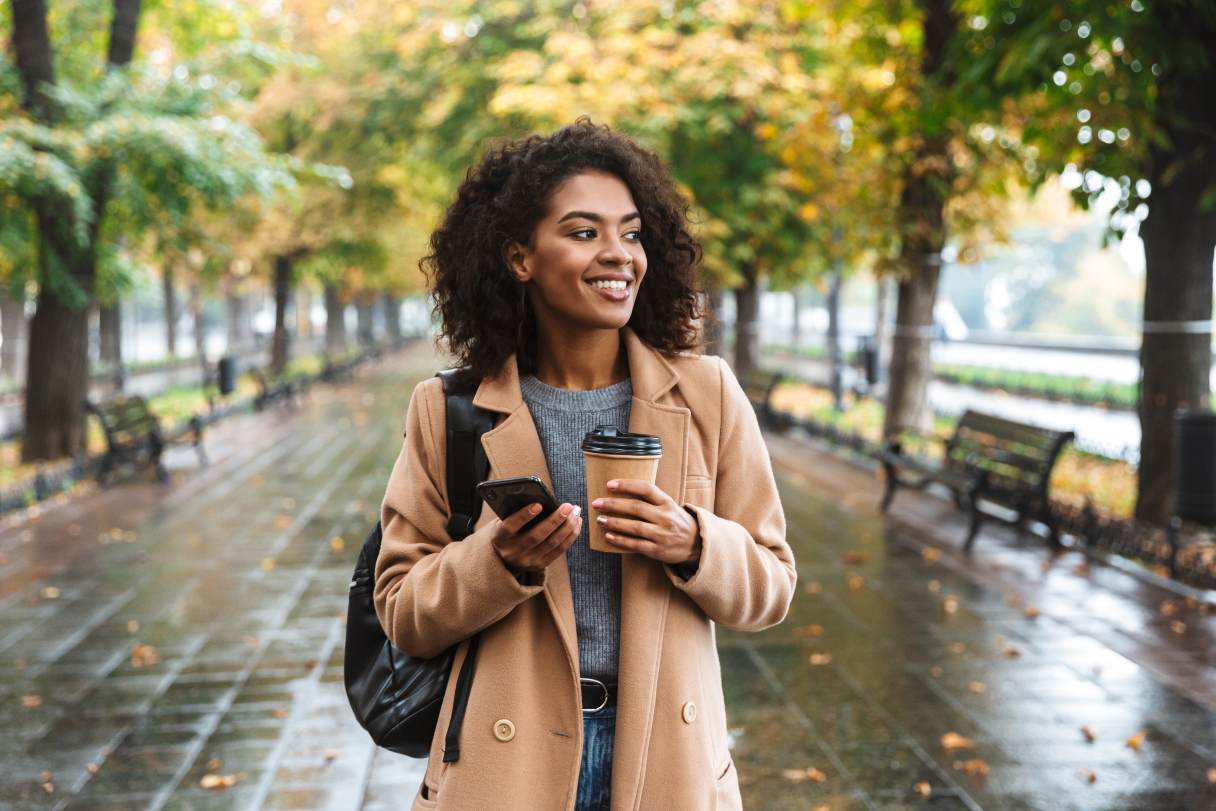 Woman holding coffee and phone, walking outside