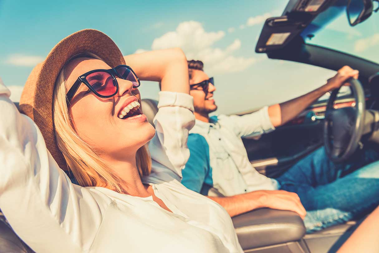 Woman in hat and sunglasses, riding in car and smiling