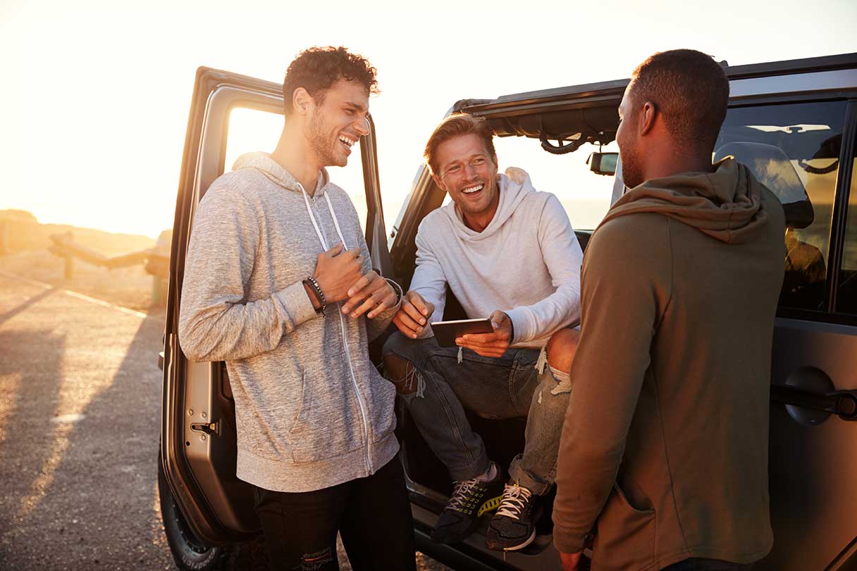 Three men conversing outside, one sitting in the driver's seat of a car