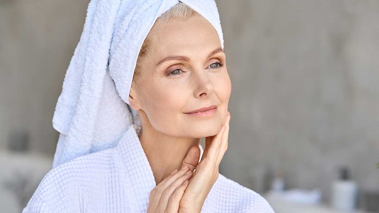 Smiling woman in robe, with towel on head, touching her face