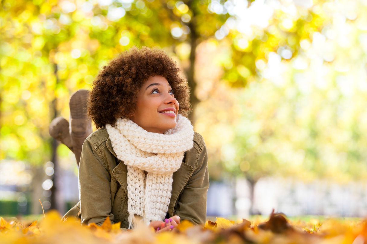 Smiling woman in scarf, laying on leaf-covered ground