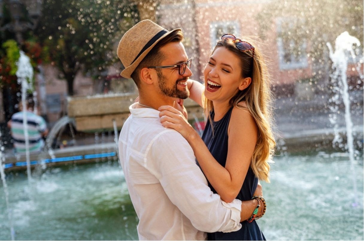 Man hugging woman in front of a fountain
