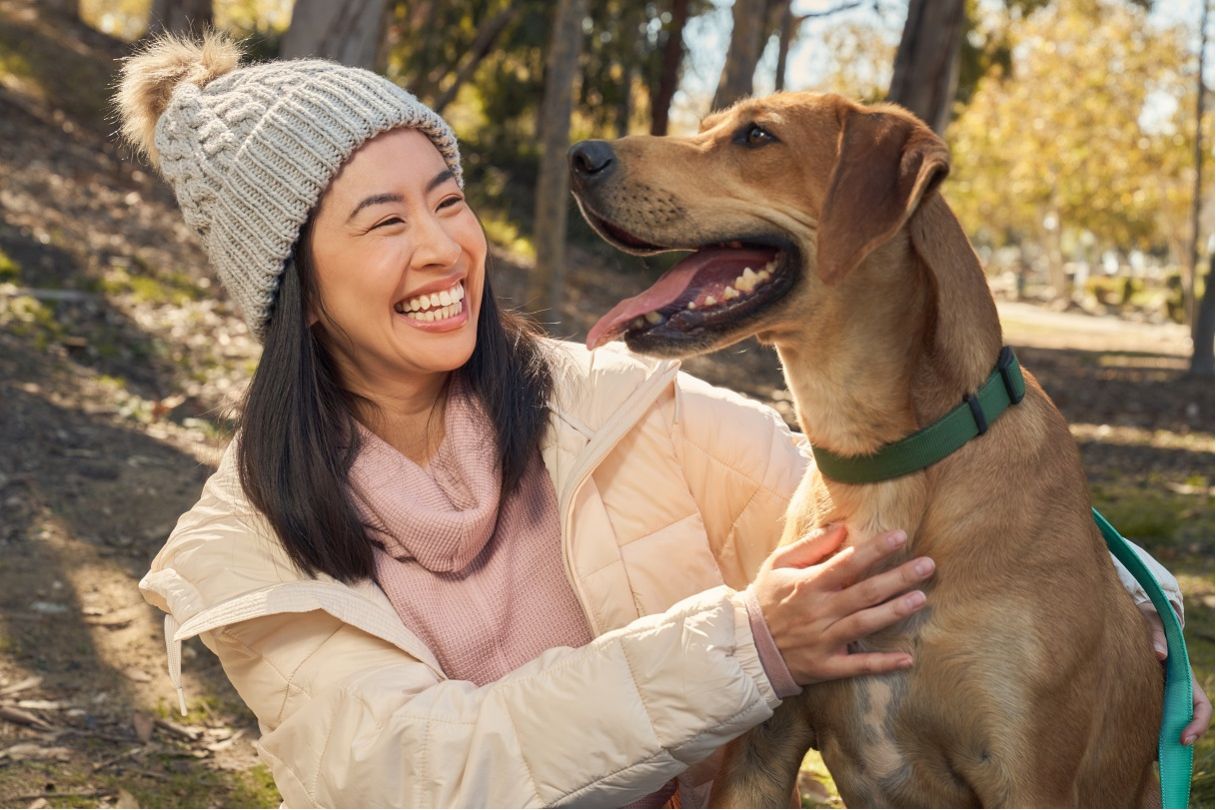 Woman with beanie on, smiling and kneeling next to dog