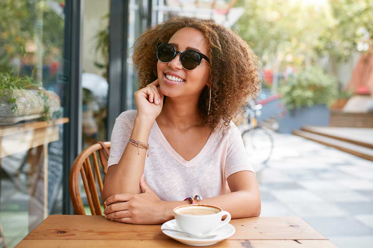 Smiling woman sitting at outdoor cafe table, wearing sunglasses