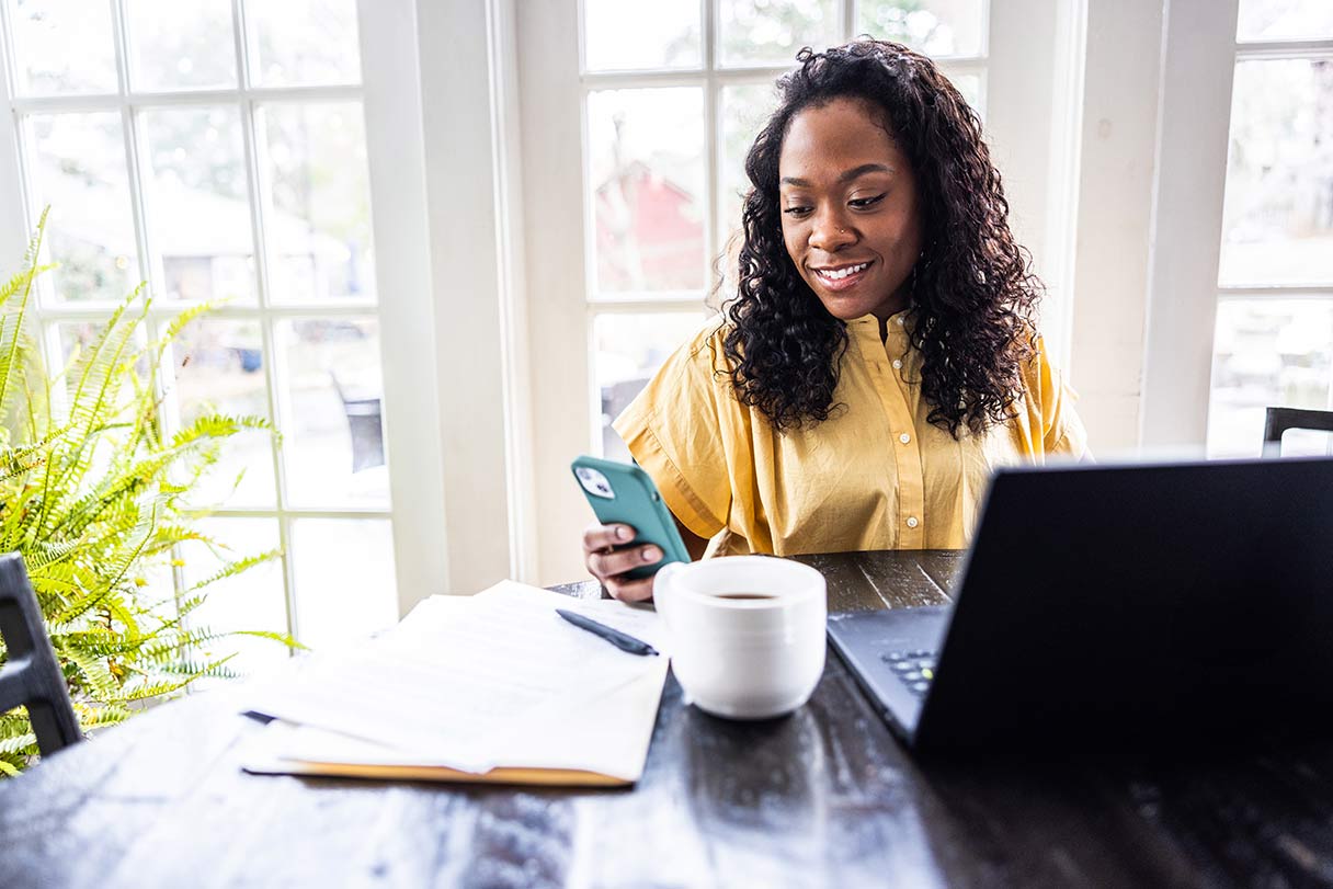 Woman working on laptop, looking at phone