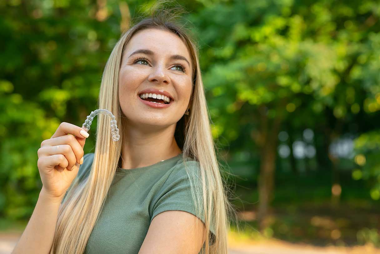 Woman smiling while holding Invisalign in front of her mouth