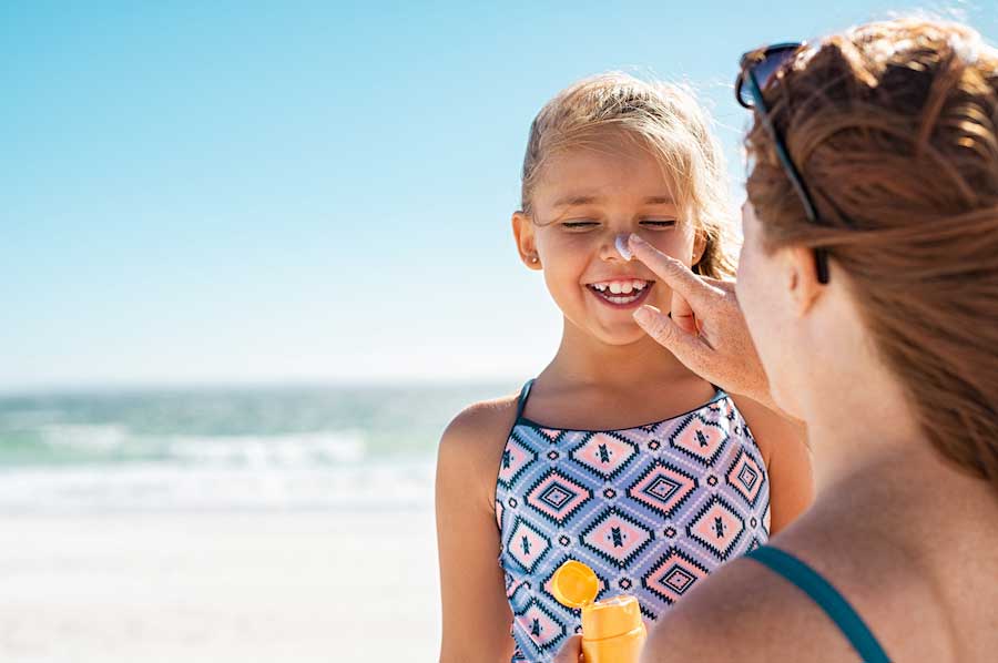 Woman on beach applying sunscreen to young girl's face