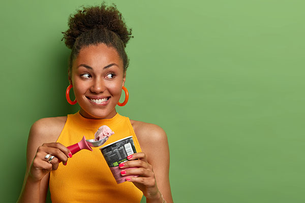Woman smiling mischievously as she eats ice cream from a pint 