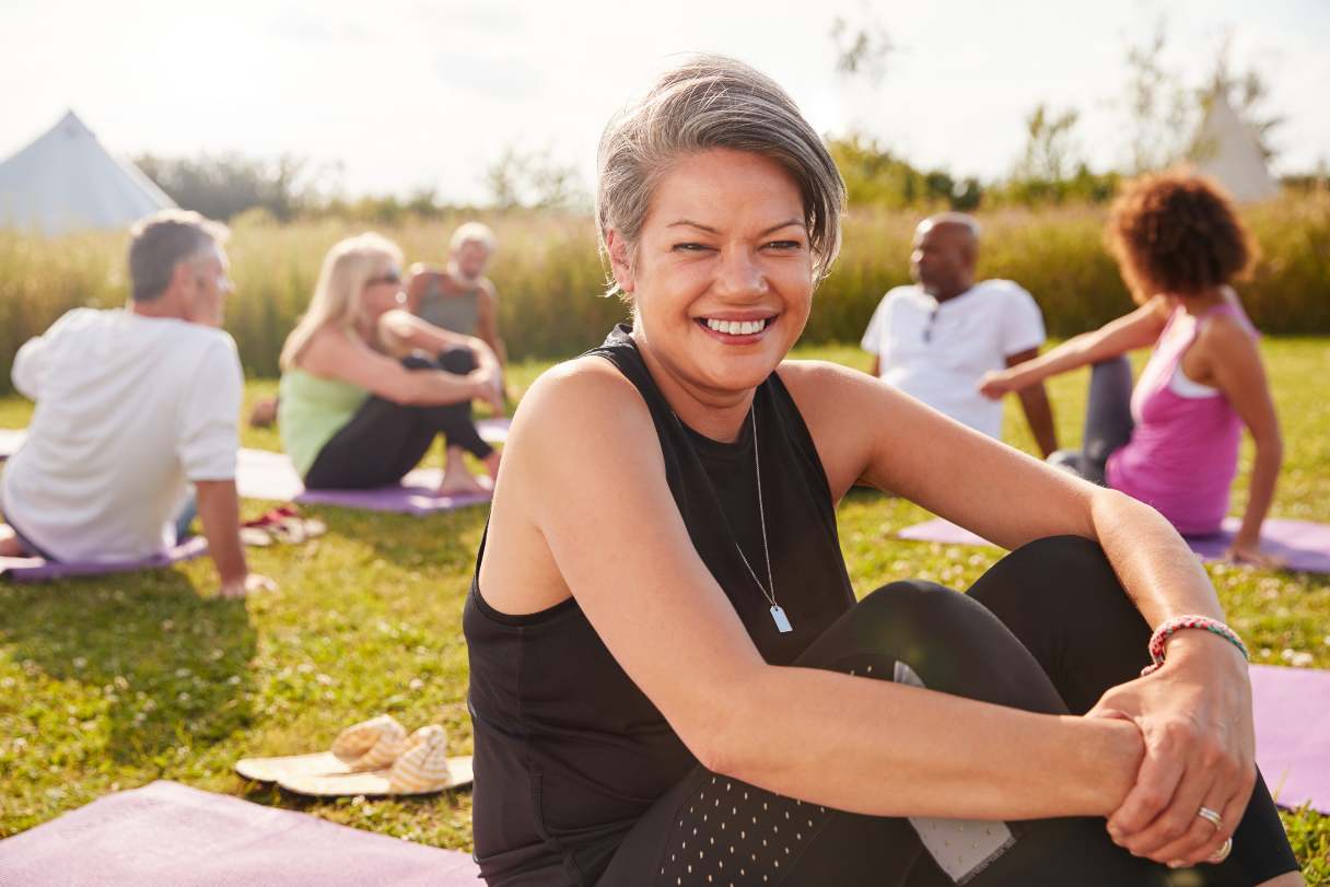 Woman smiling and sitting on yoga mat outside