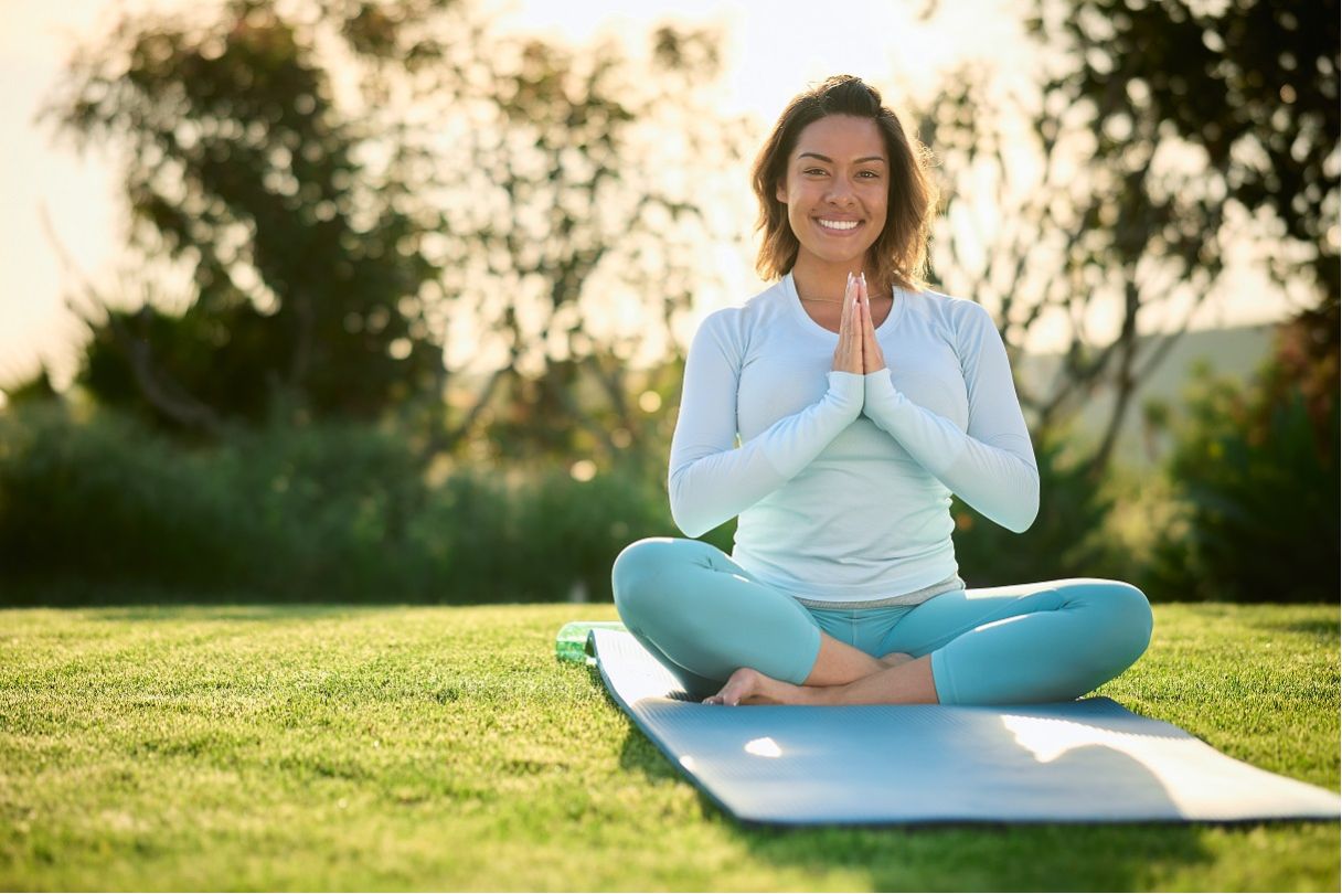 Smiling woman sitting cross-legged on yoga mat, palms pressed together