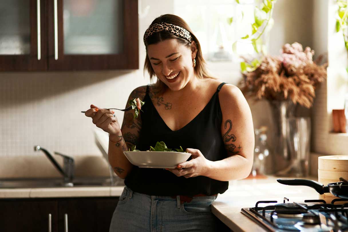 Woman in kitchen, smiling as she eats a salad