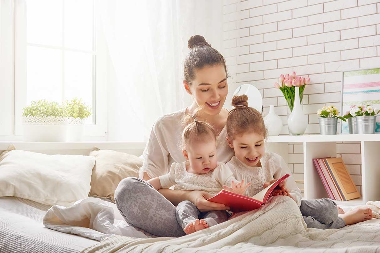 Woman sitting on a bed, reading book to her two young daughters