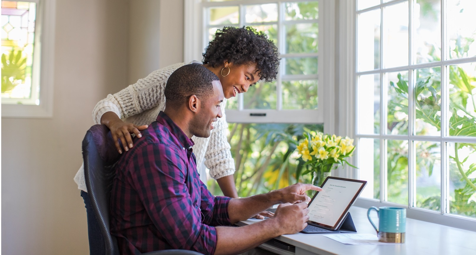 Woman smiling with hand on man's shoulder while he points at a laptop screen