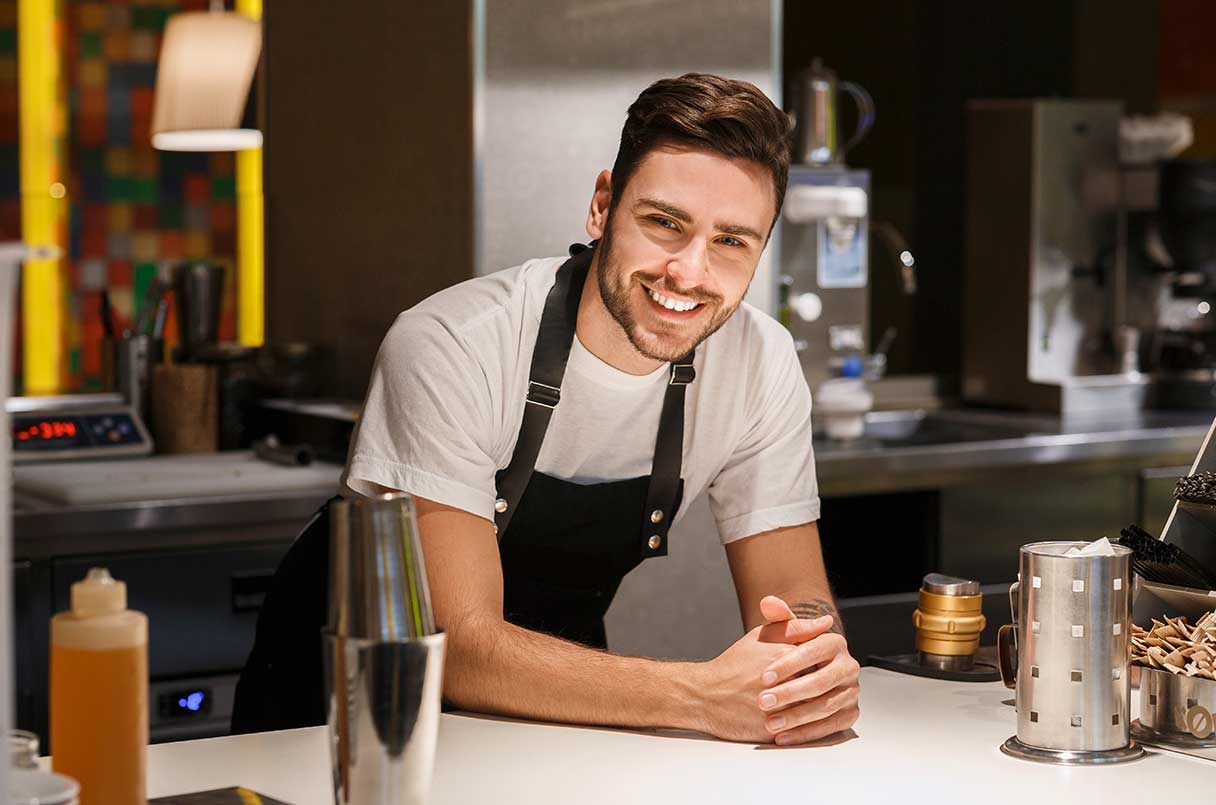 Male barista, leaning over countertop while smiling
